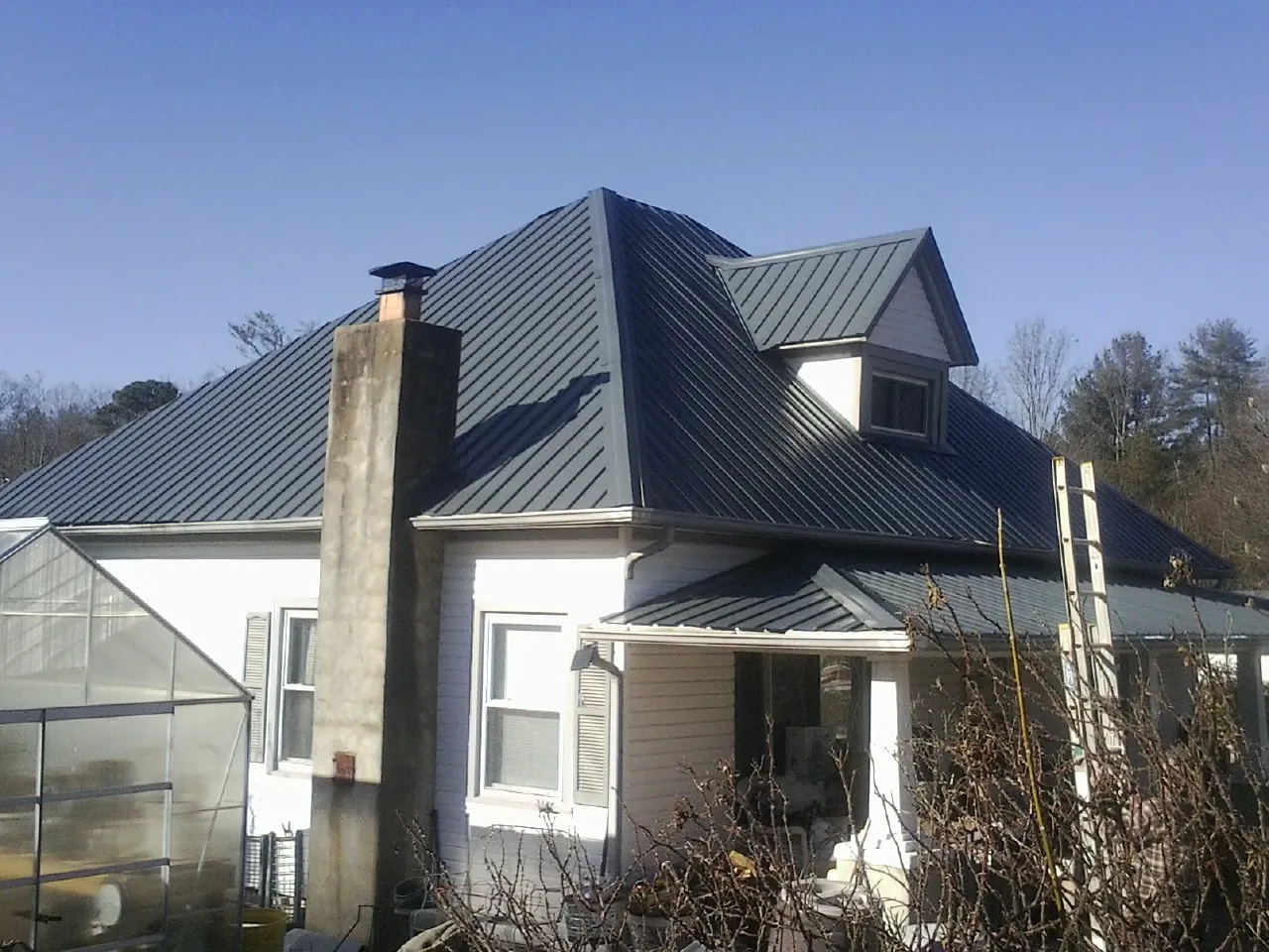 Dark blue standing seam metal roof on a white farmhouse with dormer — Slate & Tile Roof Repair by Roofing Brothers in Buies Creek