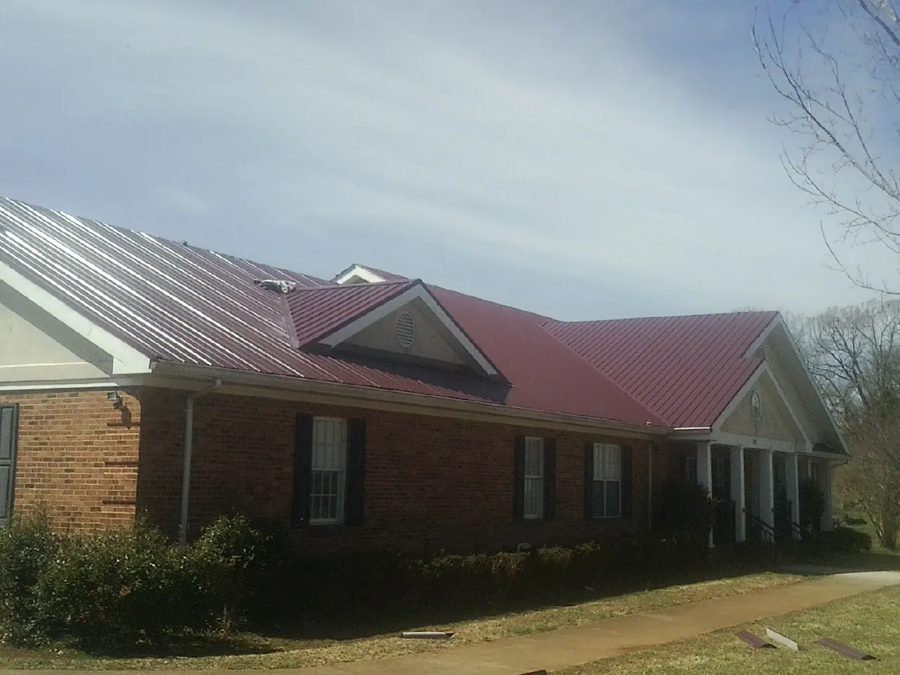 Red metal roof with gabled entries on a long brick building, from a Hail Damage Roof Repair job in Buies Creek