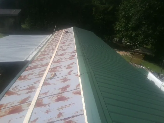 Old rusted panels beside newly installed green metal roofing — Wind Damage Roof Repair by Roofing Brothers in Buies Creek