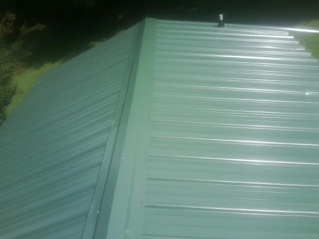 New green metal panels meeting at the ridge of a roof — Flat Roof Repair work by our crew in Buies Creek