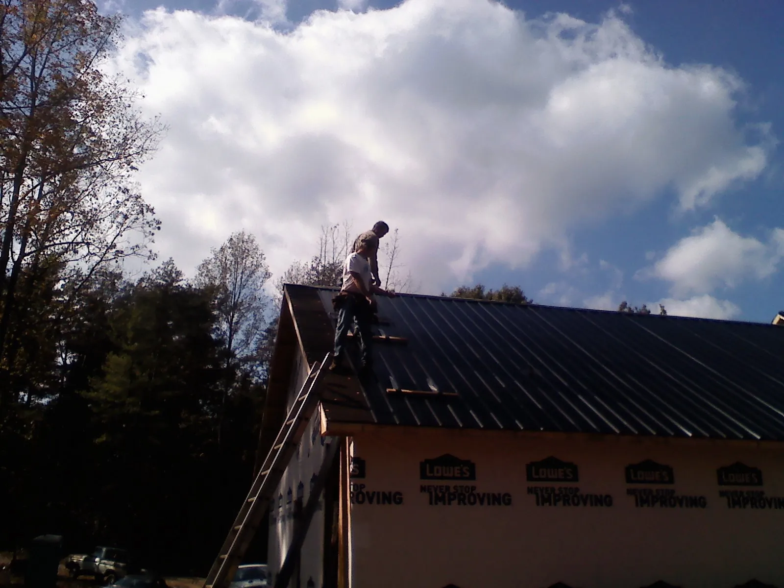 Roofer fastening dark metal panels high against a cloudy sky, from a Roof Inspection job in Buies Creek