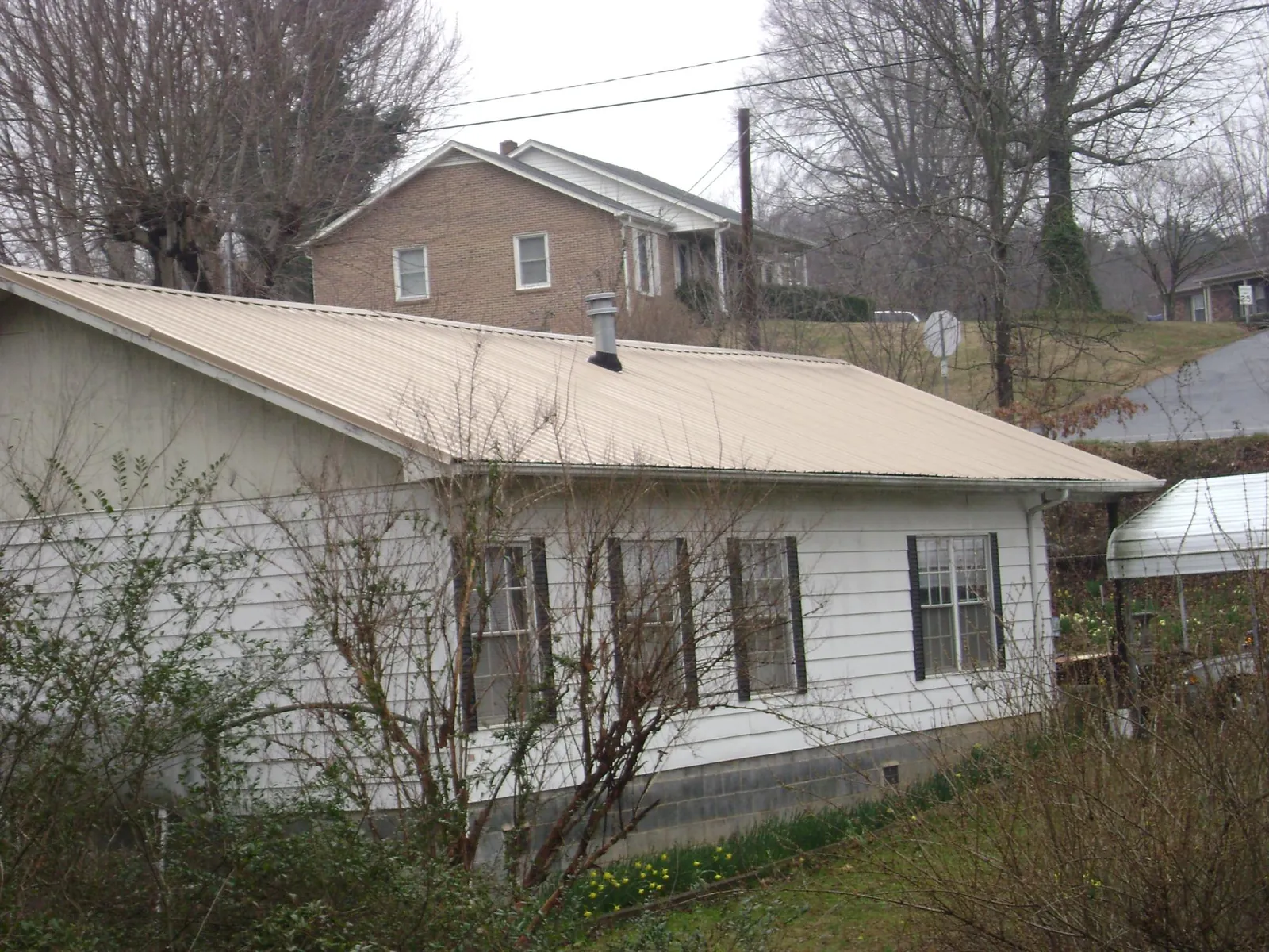 Tan metal roof on a white sided house set into a hillside — Commercial Roofing by Roofing Brothers in Buies Creek