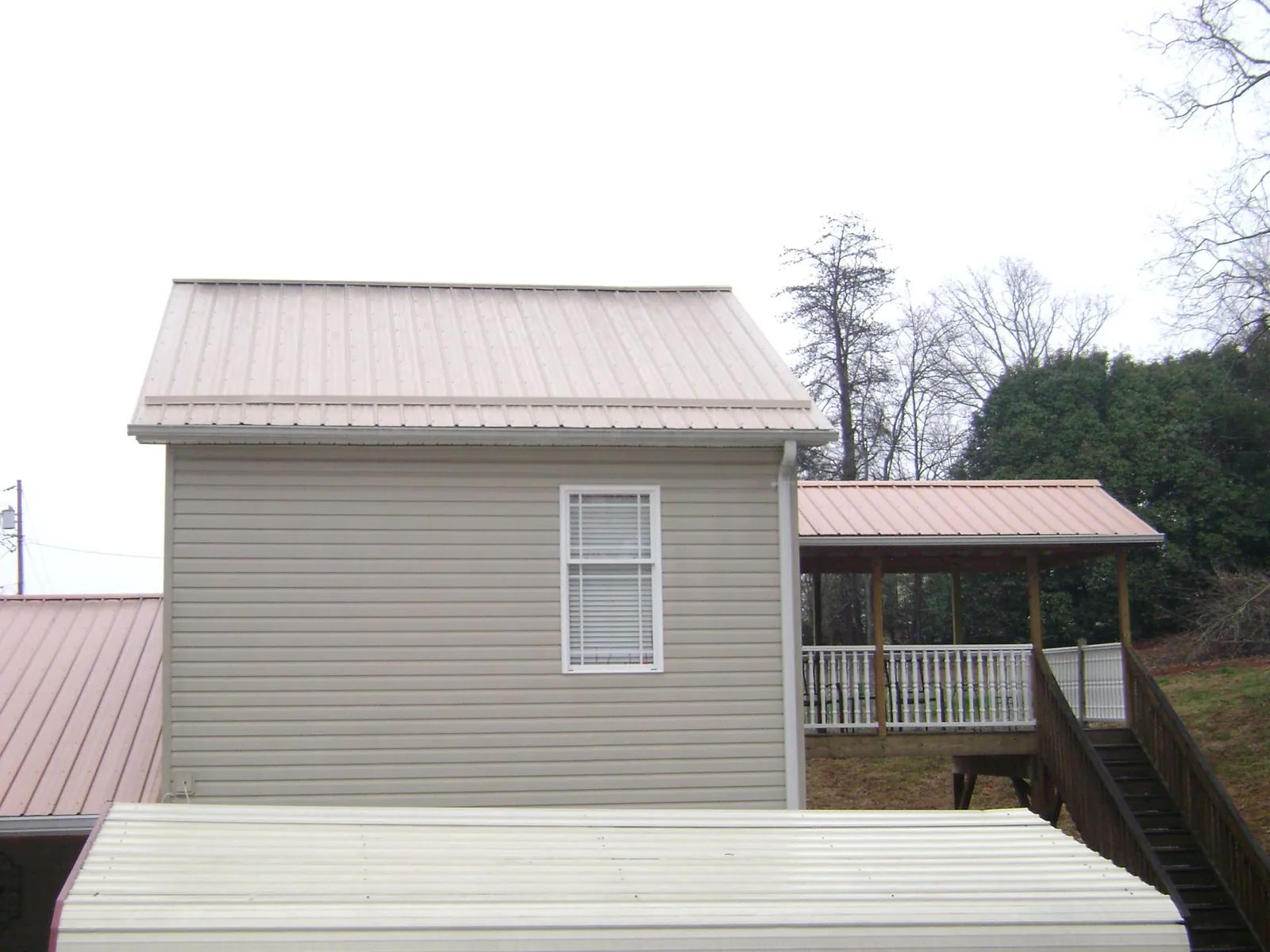 Tan metal roofs on a two story addition and attached porch, from a Roof Replacement job in Buies Creek